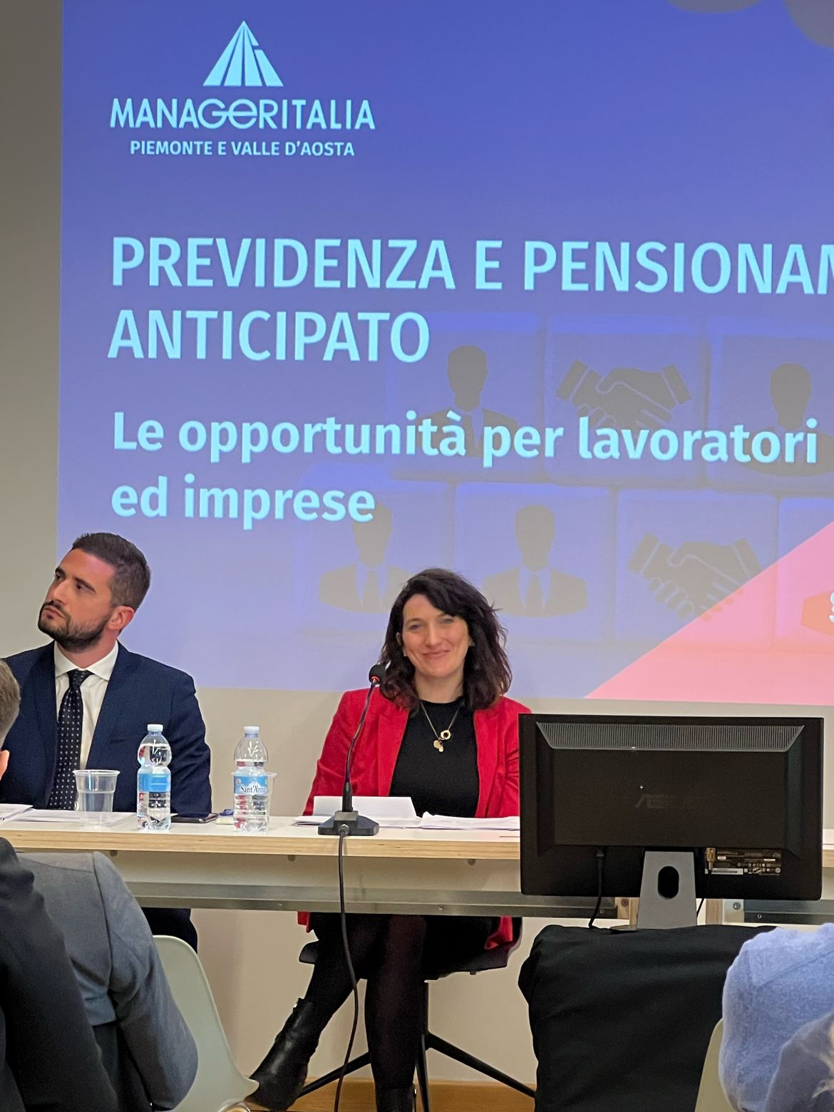 Uomo e donna dirigono una conferenza davanti ad un monitor di presentazione